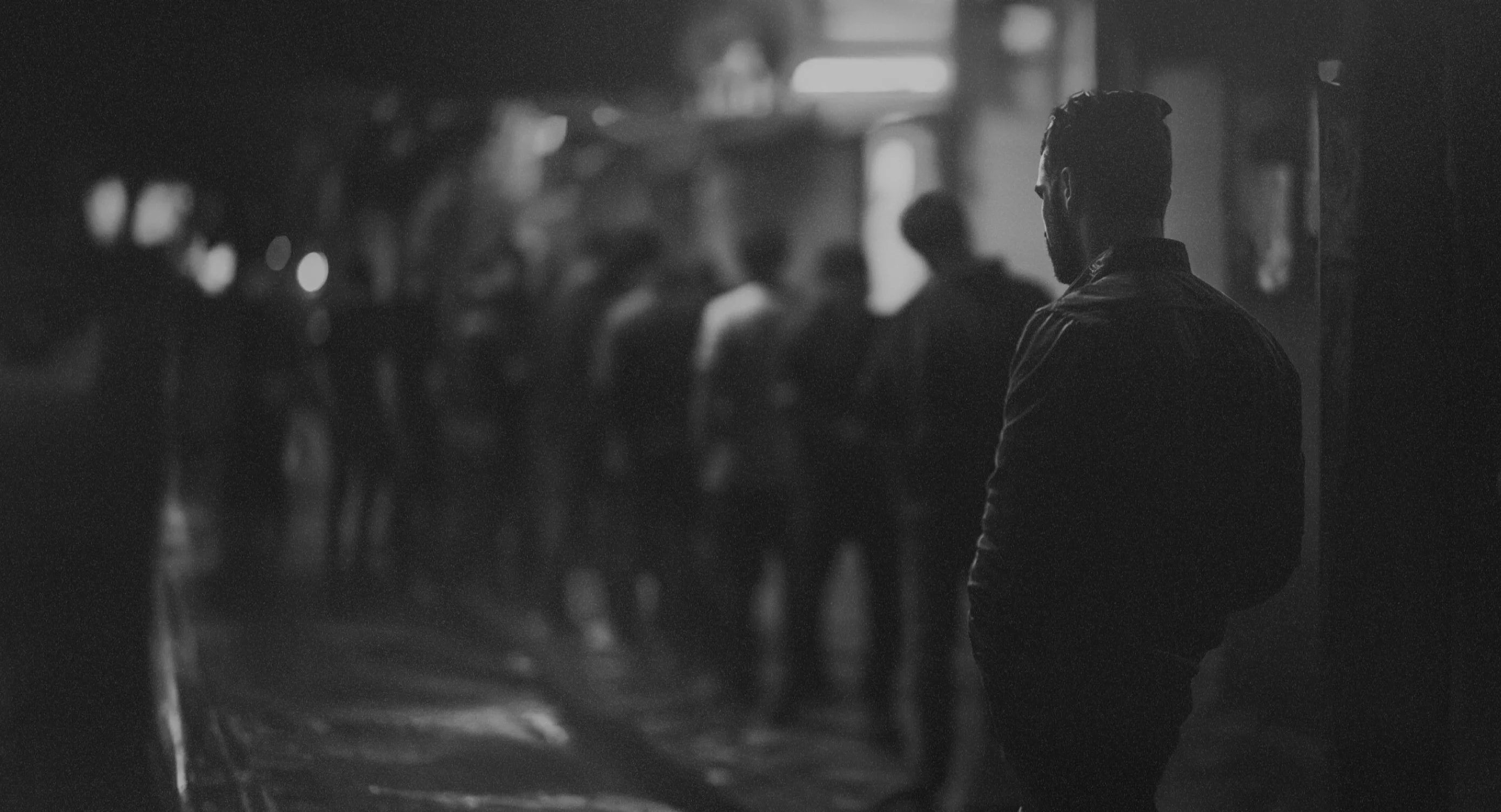 A black and white photo of a man waiting in line in a seedy part of town.