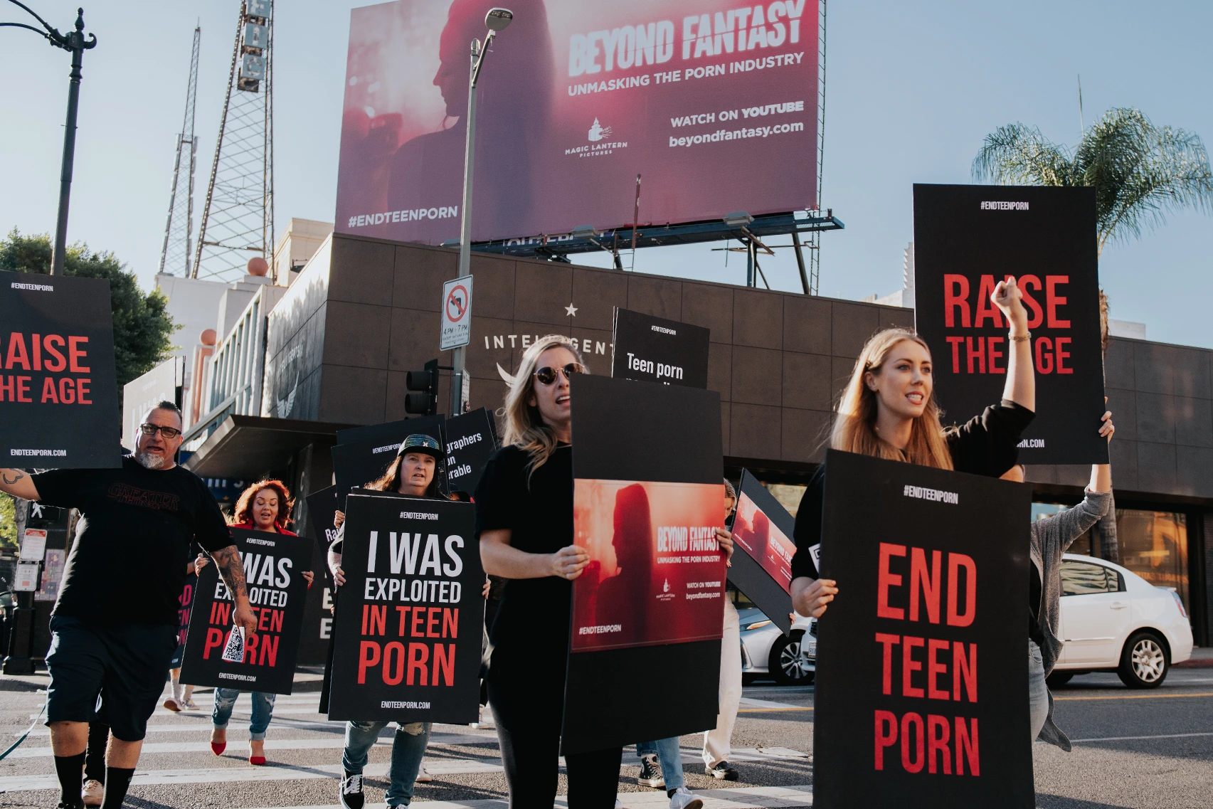 A group of women and men hold up signs in protest that say things like End Teen Porn, and 'I was exploiteded in teen porn'